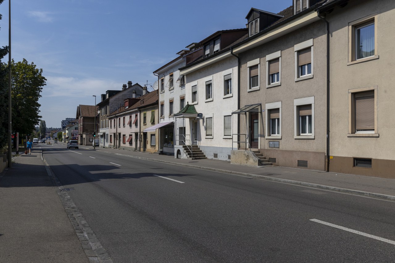 Die Binningerstrasse in ihrem heutigen Zustand: breite Asphaltfläche, Häuserzeile ohne Grünraum